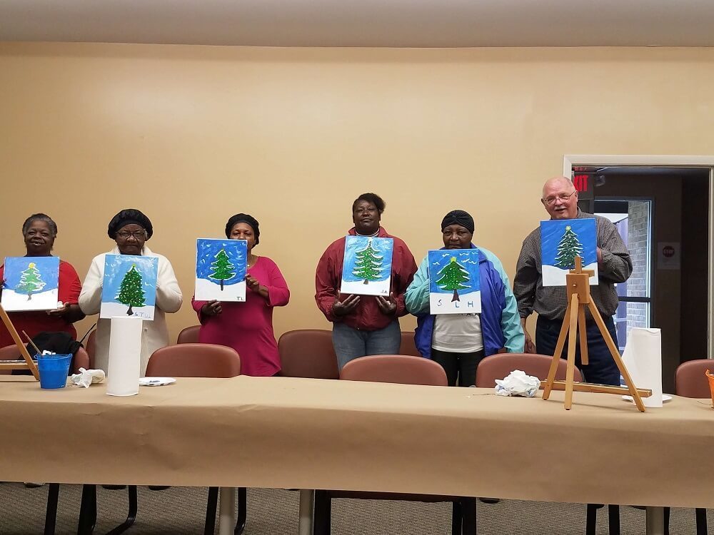 Residents of Elderly Village stand side by side showing their freshly painted canvases.