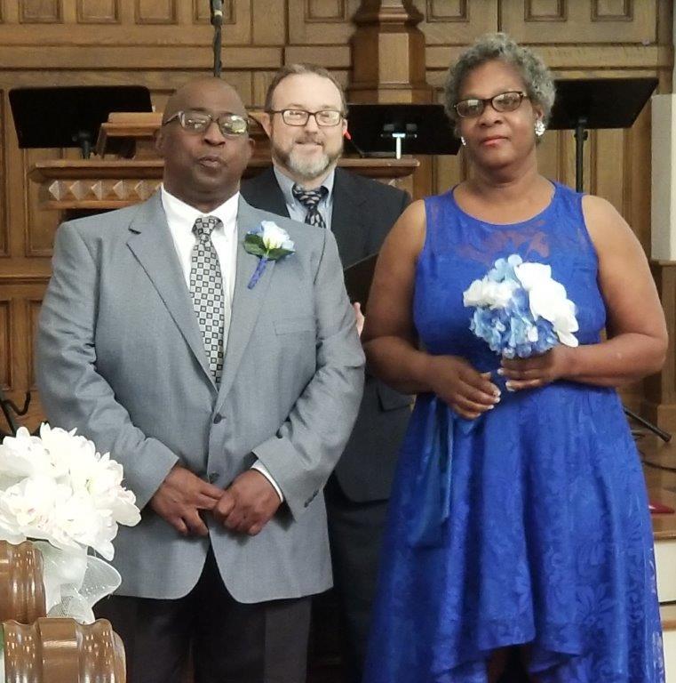 Mr and Mrs Ferguson stand together and smile with the preacher behind them. 