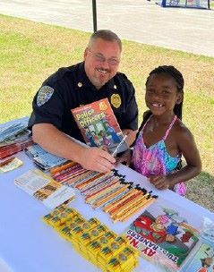 A police officer smiling with a young girl in front of school supplies.