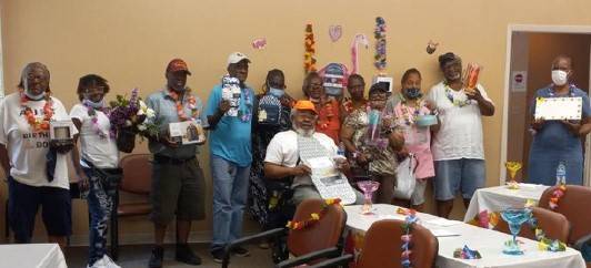 A group of elderly people in Hawaiian shirts showing their prizes after winning bingo. 