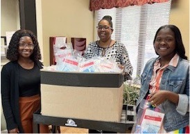 Alanna Lewis and Ambreshia Allen and other stand next to a box of pre-packaged bags.