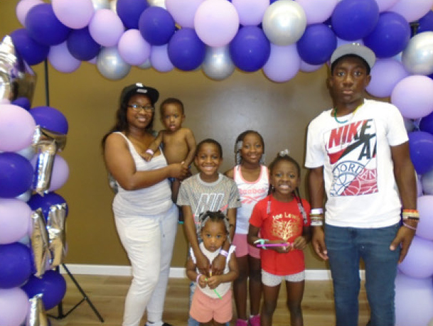 A family of 7 stands under a ballon archway. 