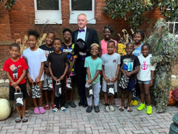A group of children stand and smile with a man in a tuxedo.