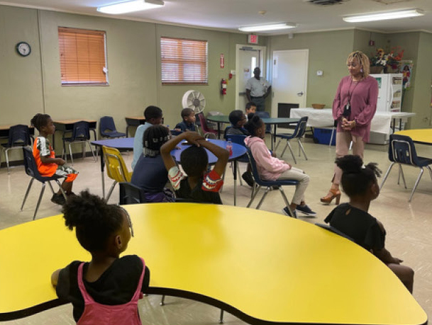 A classroom full of children are sitting and listening to their teacher.