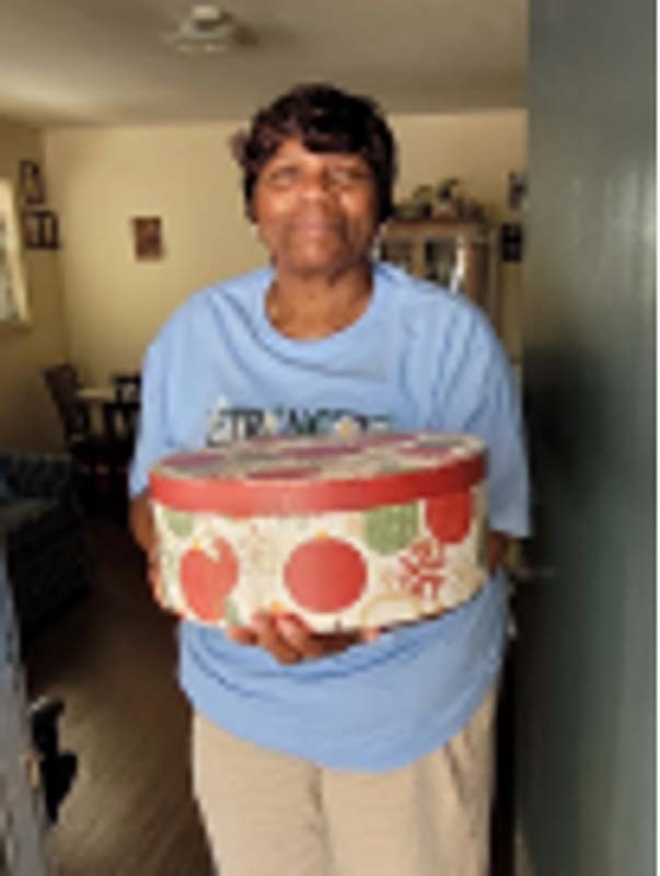An older woman stands in her apartment holding a box.