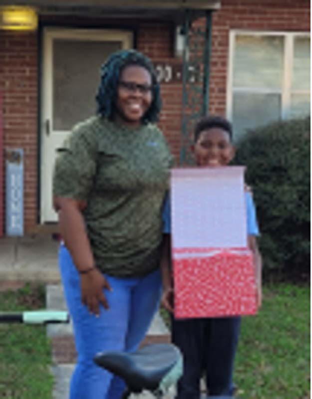 A woman and a young boy holding a box stand together. 