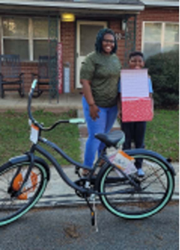 A woman and a young boy standing in the street behind his bike. The young boy is also holding a box.