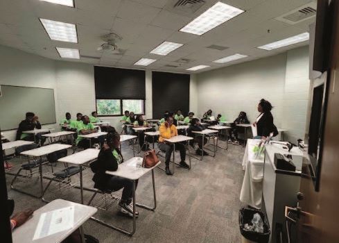 A classroom setting with a teacher and students sitting at desks. 