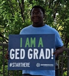 A male holding a sign with the message I am a GED Grad.