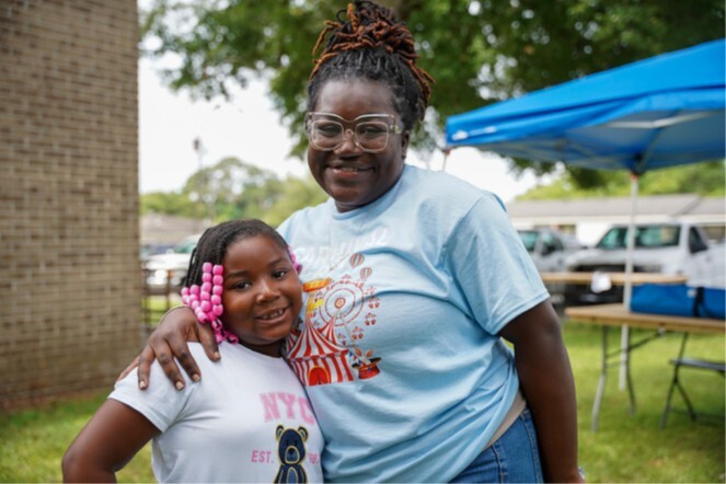 A young girl and a woman stand and smile for a picture.