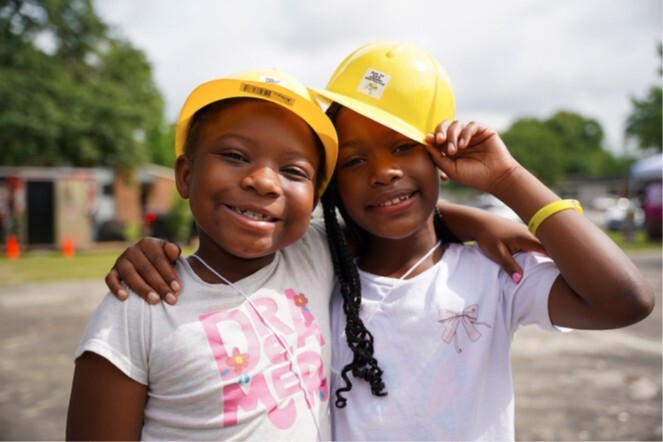 Two young girls in construction hard hats smile for a picture.