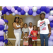 A family of 7 stands together under the balloon archway. 