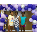 A family of three stands together under the balloon archway.