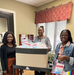 Alanna Lewis (left), Community Health Worker Ambreshia Allen (right), COVID Health Equity Navigator all stand together smiling as they pack COVID kits.