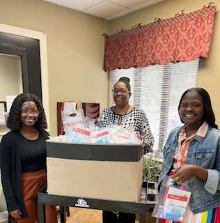 Alanna Lewis (left), Community Health Worker Ambreshia Allen (right), COVID Health Equity Navigator all stand together smiling as they pack COVID kits.