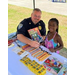A police officer is sitting at a table and handing a young girl a coloring book and pencil. 