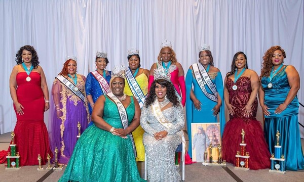 The Ms. Full Figured Pageant Queens at stand and sit together smiling.
