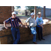 2 men and a woman are leaning against a waist height brick wall. 