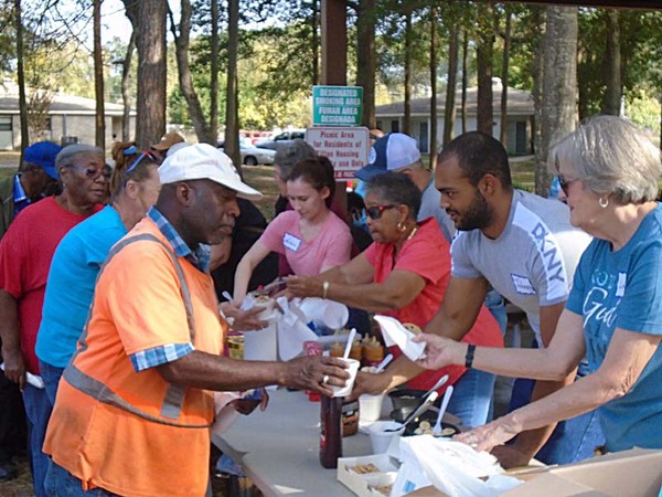 A volunteer behind the ice-cream table extends a napkin out to a resident who is holding a cup of ice-cream in his hand. 