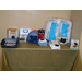 A table full of bingo prizes, including a crock-pot, waffle makers, pillows, blankets, dish towels and wash cloths, and a roasting pan. 