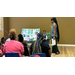  A woman describing a informational poster board to a group of people. 