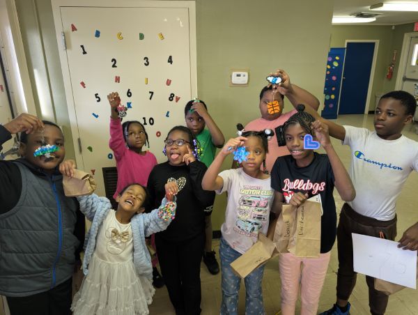 Nine kids smiling and holding up keychains that they made.