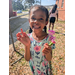  A young girl smiling holding flowers in one hand, and a lady bug on the other hand. 
