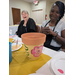  Two women smilng and laughing while looking at a flower pot with flowers painted on it. 